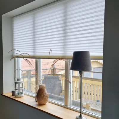 Vit plisségardin som filtrerar dagsljus i stort fönster
